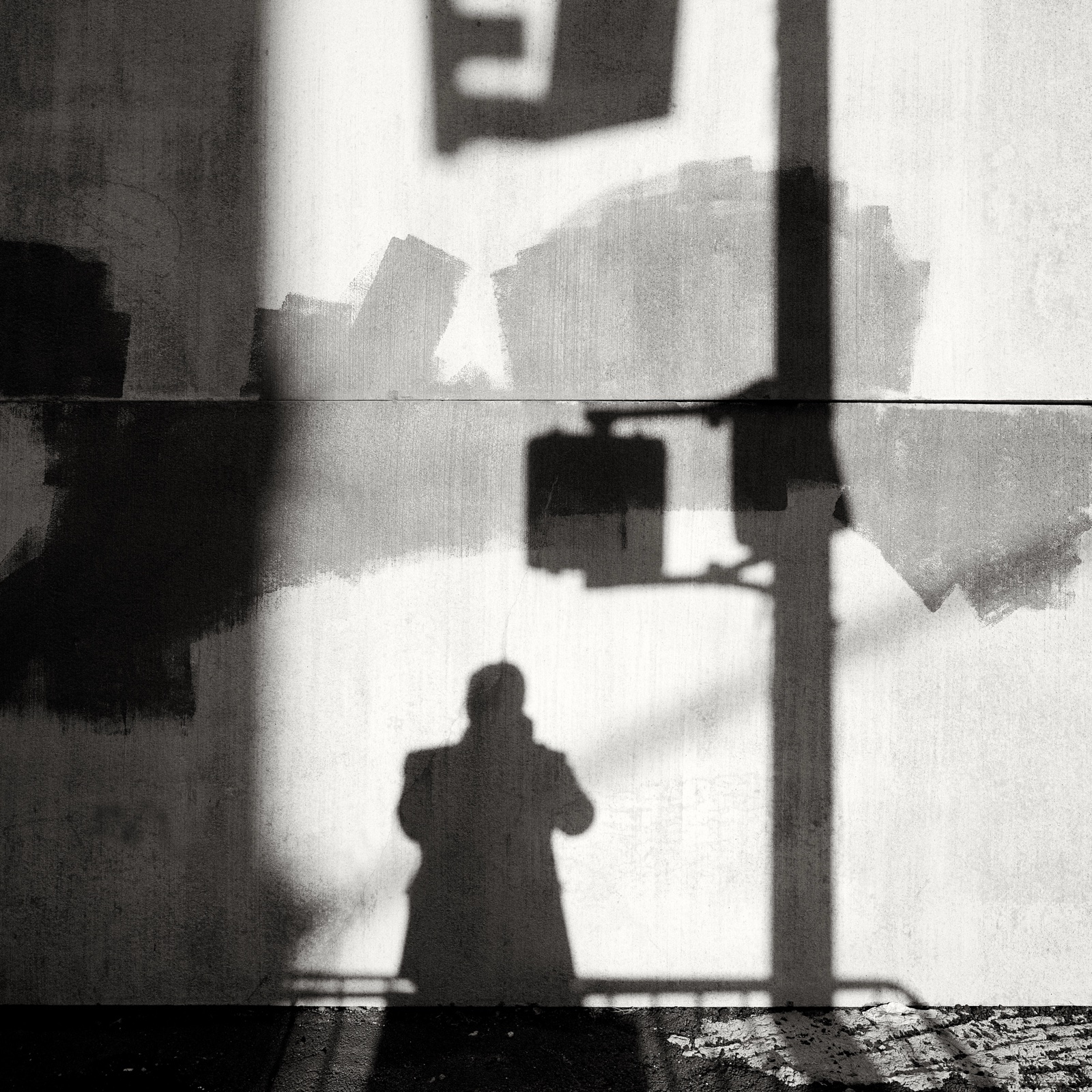 The photographer's shadow falls on a sunlit, paint-patched wall beside the shadow of a traffic signal